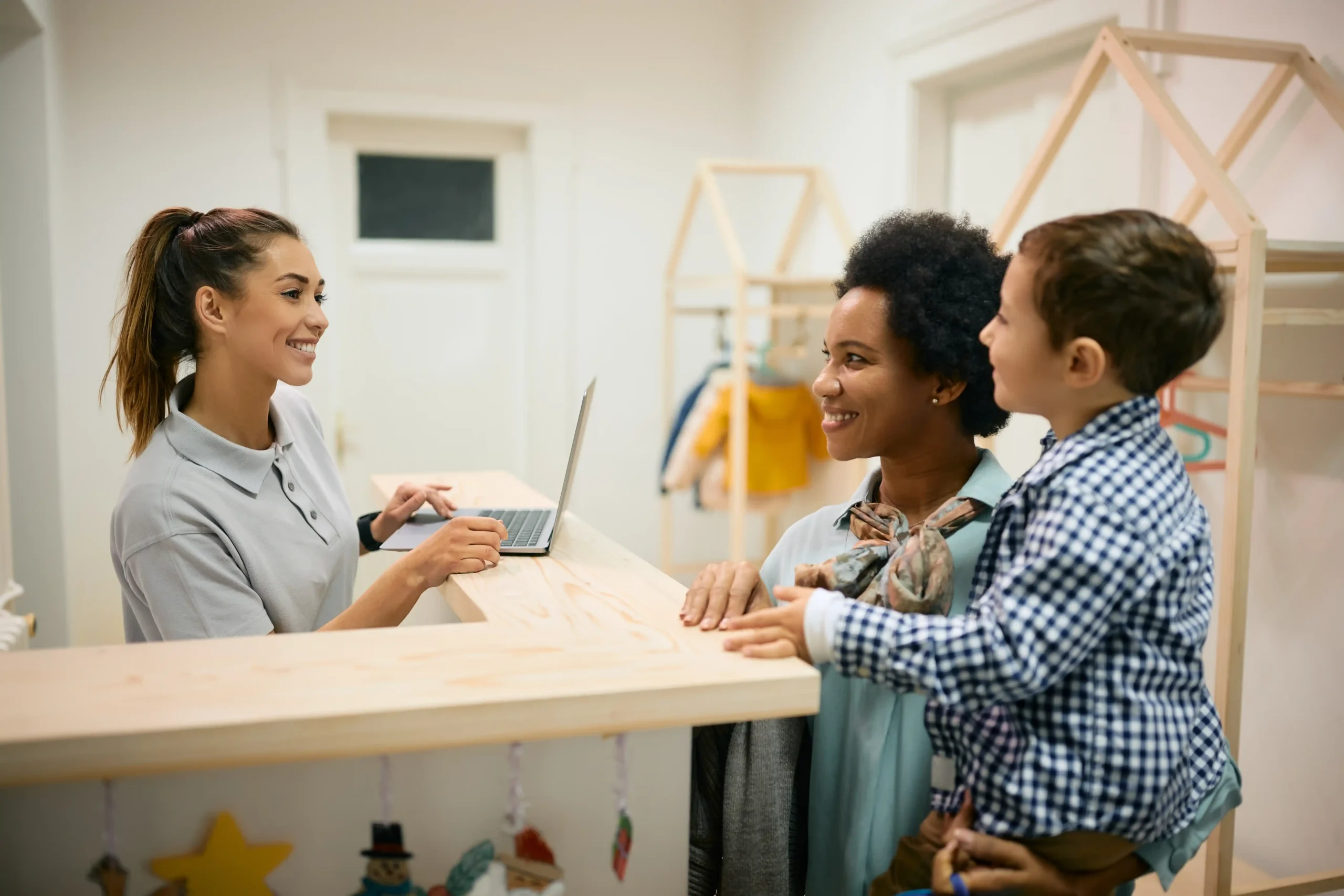 Daycare center staff member welcoming a mother and her son at the front desk for enrollment